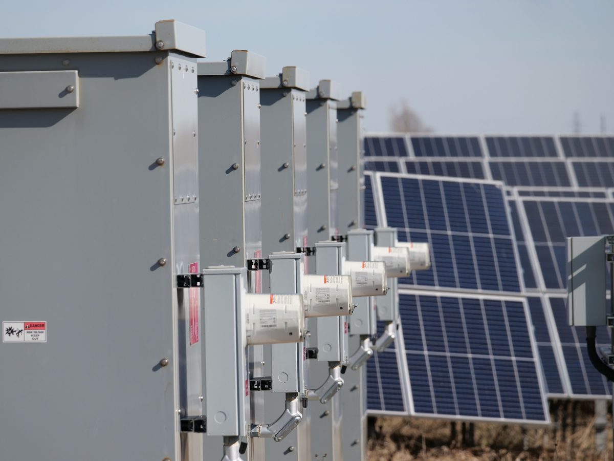 Row of solar inverters and disconnect switches beside a ground-mounted solar array