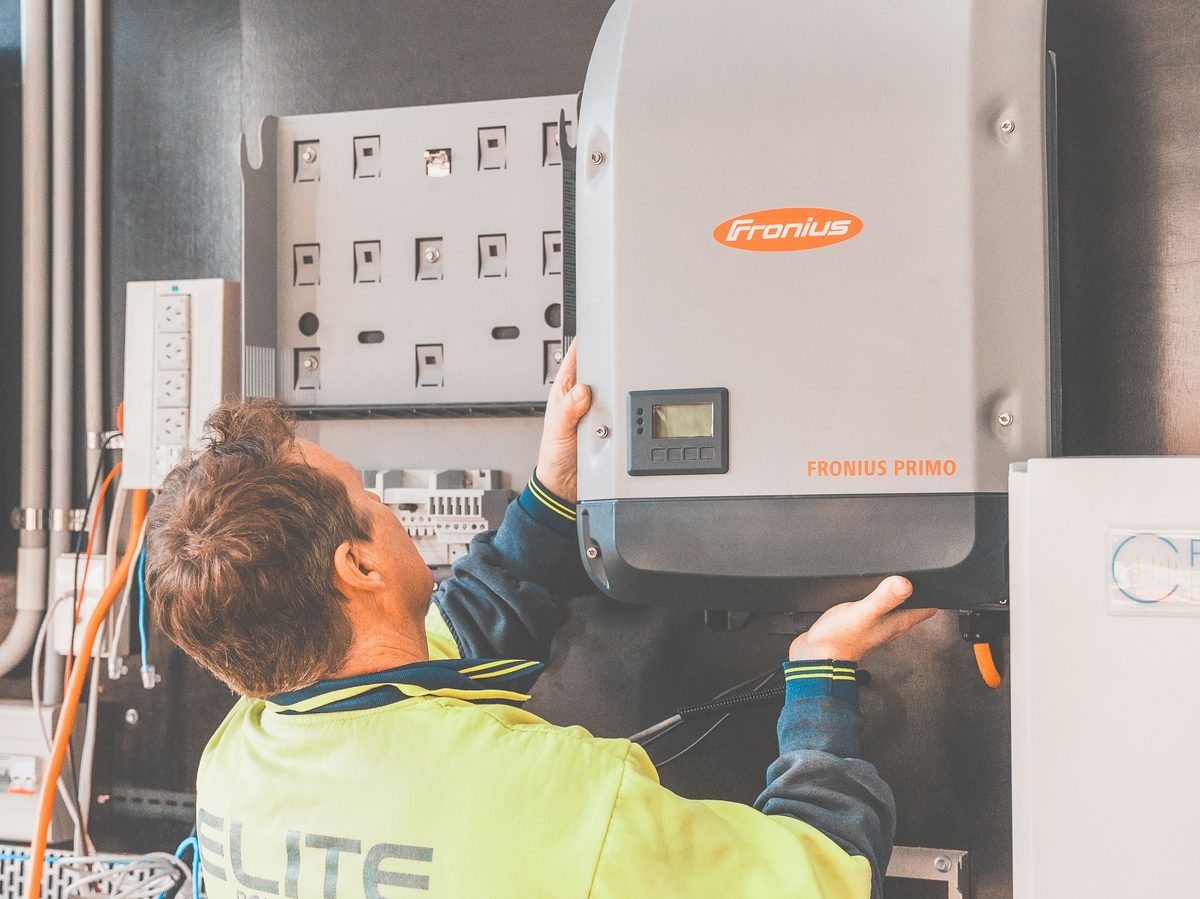 Technician working on a wall-mounted solar inverter with a visible status display screen