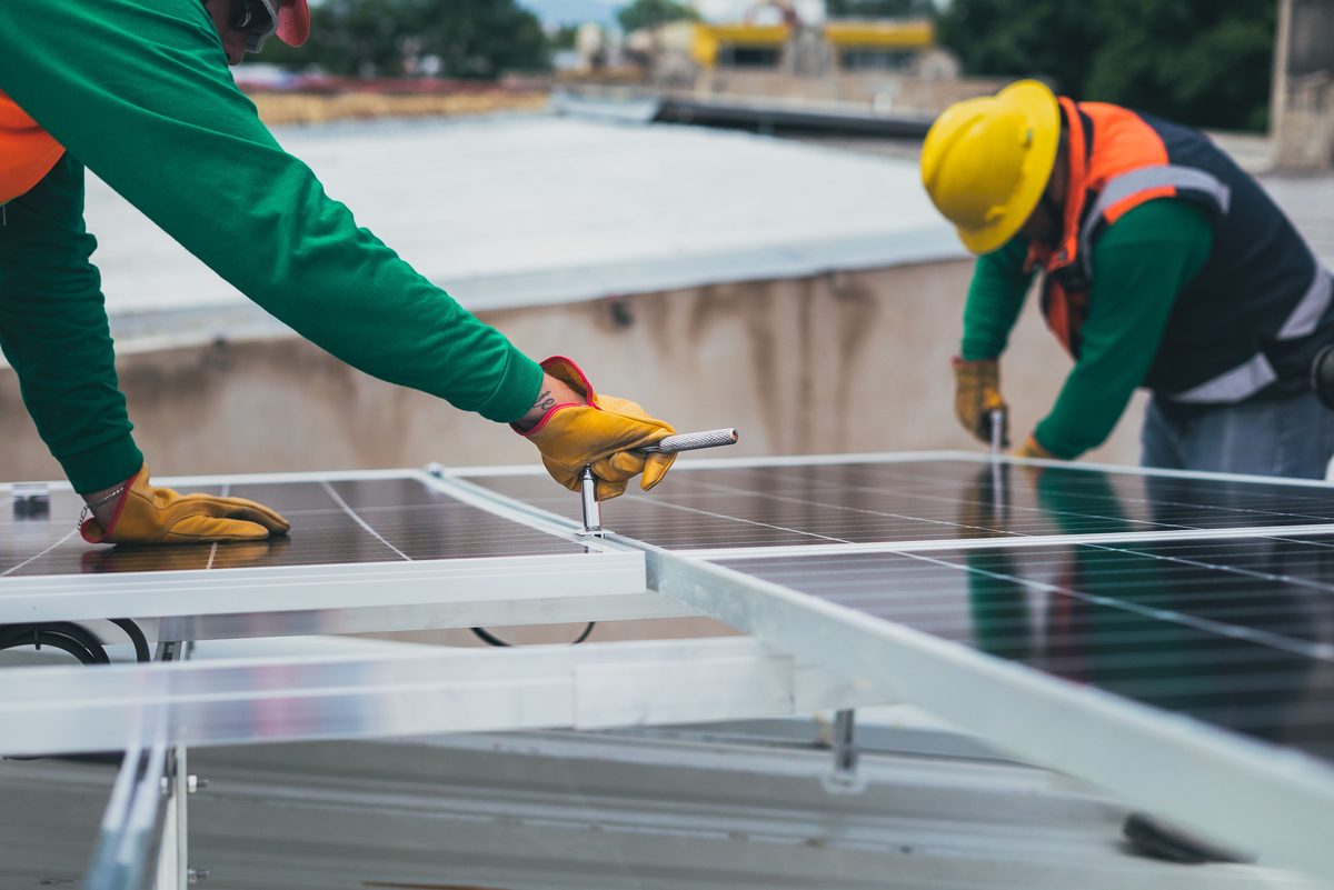 Solar installers mounting panels onto a rooftop rail system, tightening clamps with hand tools