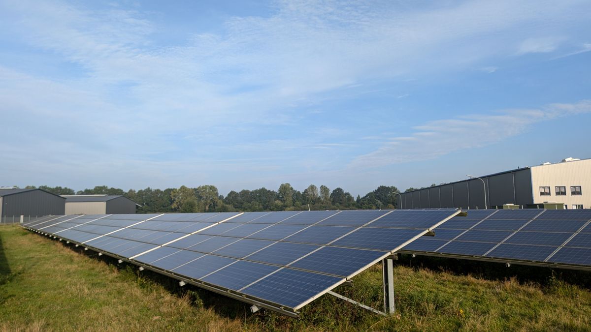 A ground-mounted solar array seen from the side, showing the panels tilted at an angle on metal frames in a grassy field
