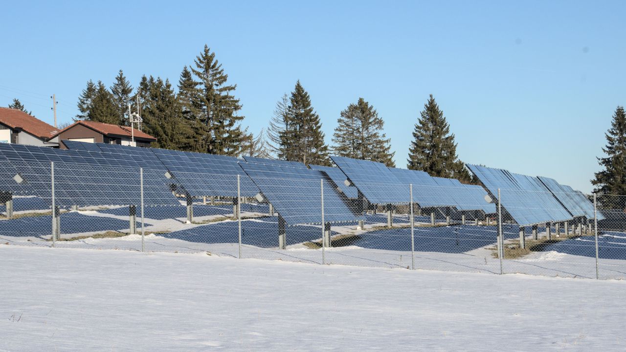A ground-mounted solar array on snow-covered ground on a cold, clear winter day